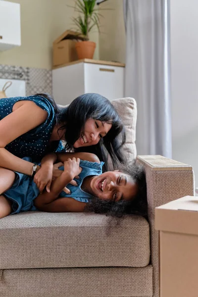 Mãe e filha multirraças se mudam para um novo apartamento. Divirta-se pulando e jogando no sofá . — Fotografia de Stock