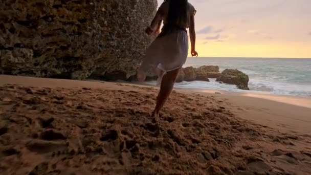 Mulher morena em um vestido que corre ao longo da água ao pôr do sol ou nascer do sol. Feliz mulher despreocupada dançando ao pôr do sol na praia. conceito de estilo de vida livre feliz . — Vídeo de Stock