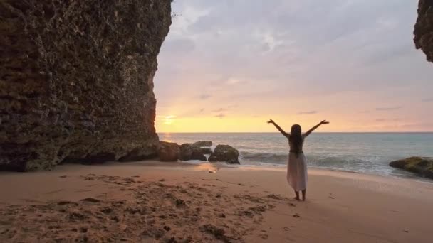 幸せな女性は海の砂の上に立って空に手を見せます被験者はぼやけてる海のそばの洞窟で喜びを表現する女. — ストック動画