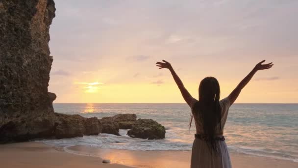 幸せな女性は海の砂の上に立って空に手を見せます被験者はぼやけてる海のそばの洞窟で喜びを表現する女. — ストック動画