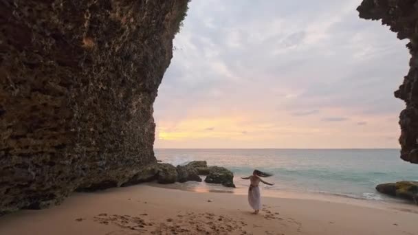 Dziewczyna biegająca po płytkiej wodzie o zachodzie słońca. Dziewczyna w białej sukience biegnie nad brzegiem morza. Jestem zadowolony z morza i plaży. Doświadczanie wolności — Wideo stockowe