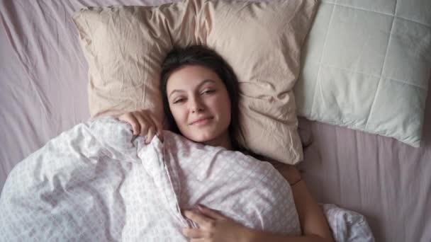 아침에 침대에 누워 손을 뻗치고 있는 한 젊은 매력적 인 여자의 정상 사진 — 비디오