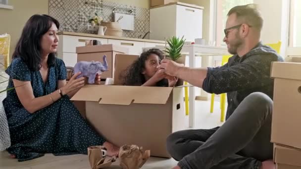 Felice etnia mista sorridente famiglia con piccolo figlio e figlia scatole di disimballaggio insieme seduti sul divano in moderno accogliente soggiorno, genitori felici che giocano con i bambini unboxing — Video Stock