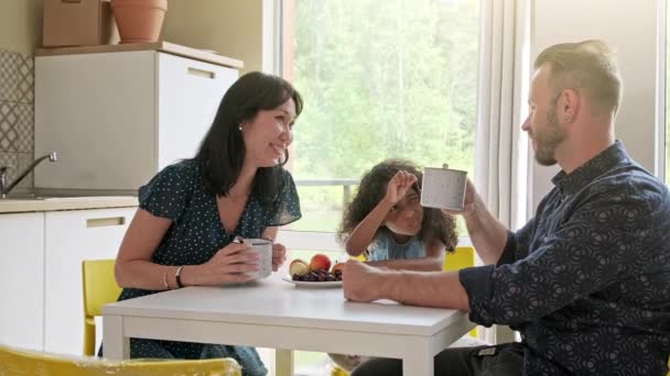 Schöne Familie mit Kind sitzt am Tisch und trinkt Kaffee im neuen Zuhause um Kartons herum — Stockvideo