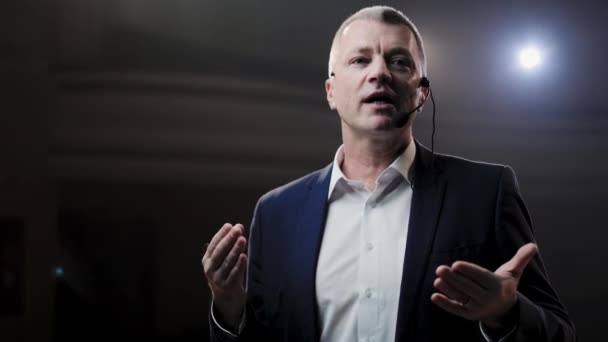 Showman. Middle Age Male entertainer, presenter or actor on stage. Arms to sides, smoke on background of spotlight. Front view portrait of a male public speaker speaking at the microphone, pointing — Stock Video