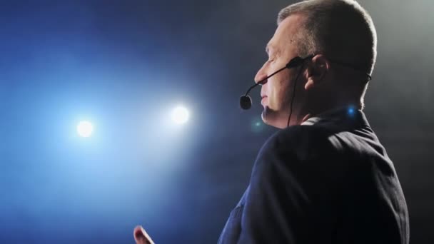 Showman. Artista, presentador o actor masculino de la Edad Media en el escenario. Brazos a los lados, humo en el fondo del foco. Vista trasera retrato de un orador público masculino hablando en el micrófono, señalando — Vídeos de Stock