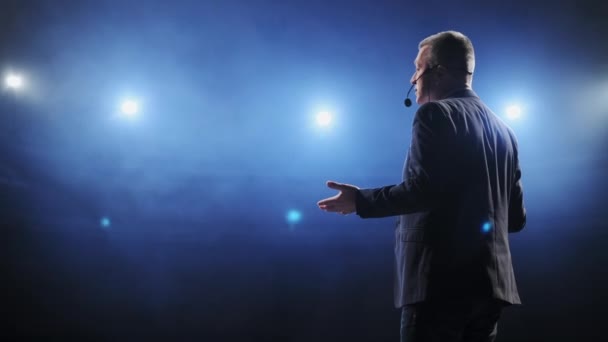 Vista posteriore di uomini che parlano attraverso un microfono nella sala conferenze buia. Un uomo parla ai microfoni in conferenza stampa. Profilo di uomo politico maturo che parla con passione da tribune — Video Stock