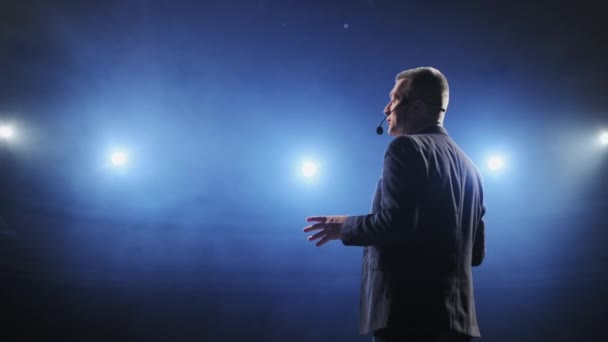 Showman. Artista, presentador o actor masculino de la Edad Media en el escenario. Brazos a los lados, humo en el fondo del foco. Vista trasera retrato de un orador público masculino hablando en el micrófono, señalando — Vídeos de Stock