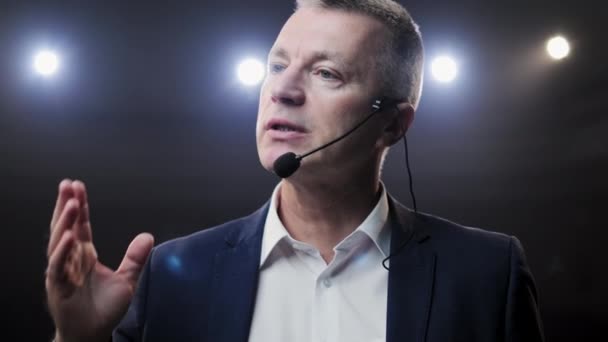 Portrait d'hommes parlant à travers un micro dans une salle de conférence sombre. L'homme parle dans les microphones lors de la conférence de presse. Profil d'un homme politique mature parlant passionnément de tribune — Video