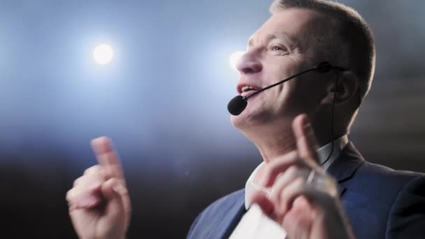 Showman. Middle Age Male entertainer, presenter or actor on stage. Arms to sides, smoke on background of spotlight. Front view portrait of a male public speaker speaking at the microphone, pointing — Stock Video