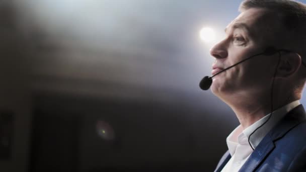 Showman. Middle Age Male entertainer, presenter or actor on stage. Arms to sides, smoke on background of spotlight. Front view portrait of a male public speaker speaking at the microphone, pointing — Stock Video