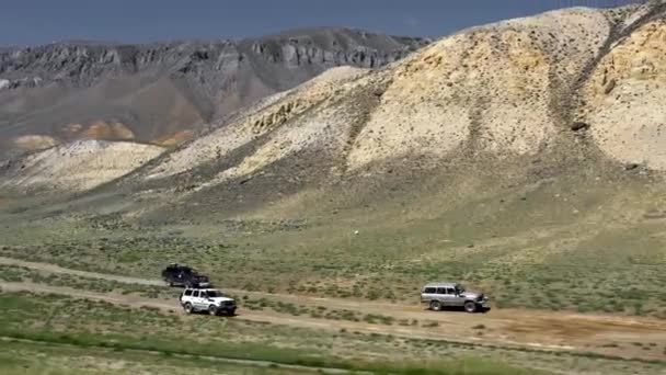 观看在沙道上行驶的狩猎车。 四轮驱动汽车沿着干旱的沙漠山脉附近的砾石小径行驶。帕米尔公路丝绸之路探险 — 图库视频影像
