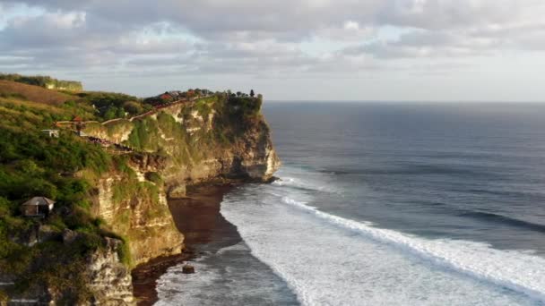 Fantastisk utsikt över höga klippor ovanför blå hav. Silhuett av Uluwatu tempel på klippan toppen. Bali, Indonesien — Stockvideo