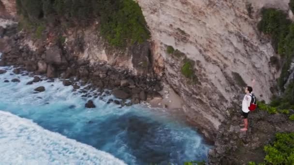 Úspěšný mladý muž silueta stojící na útesu oceánu letecké zvedání zbraní štěstí radost svoboda koncepce — Stock video