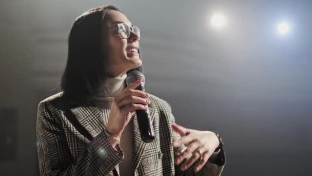 The female financial coach emotional gesturing talks from the stage with spectators at forum. Too many anonymous persons workers and students seat in large auditorium and watch workshop background — Stock Video