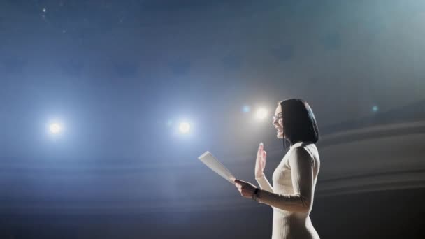 La entrenadora financiera habla emocionalmente desde el escenario con los espectadores en el foro. Demasiadas personas anónimas trabajadores y estudiantes se sientan en un gran auditorio y observan los antecedentes del taller — Vídeo de stock