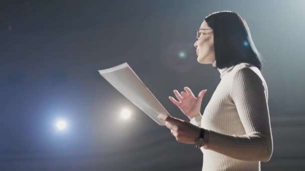 L'allenatore finanziario femminile gesti emotivi colloqui dal palco con gli spettatori al forum. Troppe persone anonime lavoratori e studenti siedono in un grande auditorium e guardano lo sfondo del workshop — Video Stock