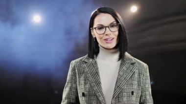 Şov kadını. Kadın şovmen, sunucu ya da oyuncu. Kollar yana, arka planda duman. Mikrofona konuşan bir erkek konuşmacının ön manzara portresi.