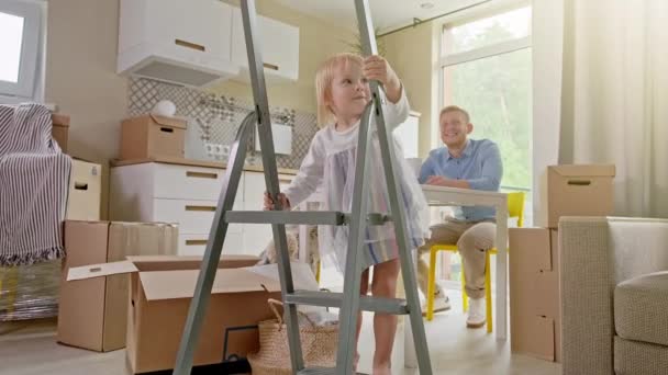 房屋出租中的活跃家庭团体搬迁. 积极看待玩具家庭重新安置或拆开纸箱包装的问题。 小女孩爬上楼梯，看着摄像机. — 图库视频影像