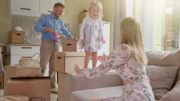 Aktive Familiengruppe zieht in Mietimmobilien um. Positiv sieht er das Um- oder Auspacken von Kartons durch eine verspielte Familie. kleines Mädchen springt auf Händen zu Mama. Leben oder Traum genießen — Stockvideo