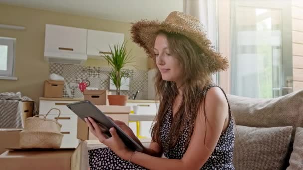 Woman using tablet with boxes at the back. Portrait of young beautiful woman with mobile phone in her new house — Stock Video