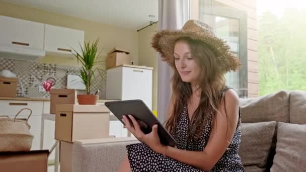 Wanita menggunakan tablet dengan kotak di belakang. Potret wanita cantik muda dengan ponsel di rumah barunya — Stok Video