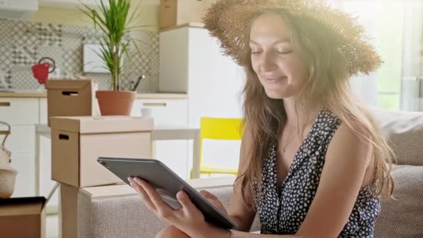 Femme utilisant une tablette avec des boîtes à l'arrière. Portrait de jeune belle femme avec téléphone portable dans sa nouvelle maison — Video