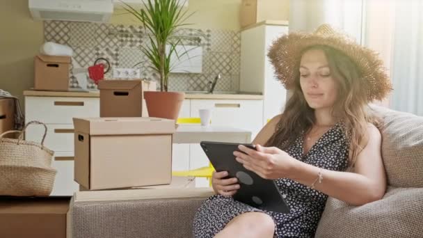 Woman using tablet with boxes at the back. Portrait of young beautiful woman with mobile phone in her new house — Stock Video