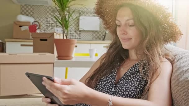 Wanita menggunakan tablet dengan kotak di belakang. Potret wanita cantik muda dengan ponsel di rumah barunya — Stok Video