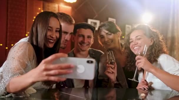 Joven alegre amigas tomando selfie en pub usando el teléfono. Amigos, hombres, mujeres, ocio, amistad y concepto de tecnología: amigos con teléfonos inteligentes que beben cerveza en el bar o pub — Vídeo de stock