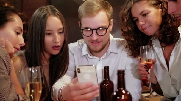 Compagnie d'amis hipster focalisés utilisant le téléphone intelligent dans le bar, pub tandis que l'homme caucasien commencent à célébrer la victoire à la loterie et montrant le téléphone intelligent aux amis . — Video