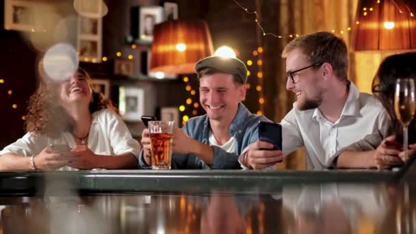 Retrato de grupo de estudantes felizes hipster assistindo vídeo, foto no telefone inteligente juntos enquanto sentados na mesa de madeira no bar moderno, pub . — Vídeo de Stock