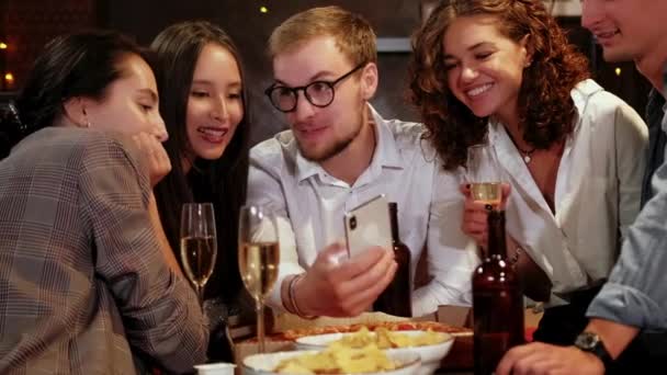 Company of focused hipster friends using smart phone in the bar, pub while caucasian man start celebrating win in the lottery and showing smart phone to the friends. — Stock Video