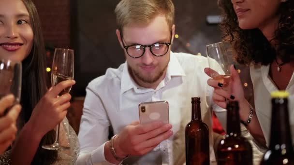 Amigos en un pub celebran y se divierten, un tipo está mirando un teléfono inteligente, y no hablar con otras personas. El problema de la sociedad moderna . — Vídeo de stock