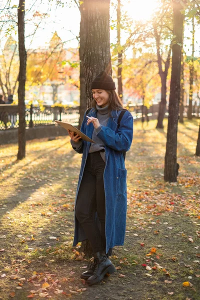 Όμορφη νεαρή μαθήτρια σπουδάζει χρησιμοποιώντας ένα τάμπλετ σε ένα πάρκο. Ψυχαγωγία και μελέτη — Φωτογραφία Αρχείου