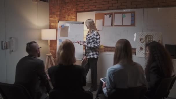 Vrouwelijke manager presenteert nieuw projectplan aan collega 's op vergadering, het uitleggen van ideeën over flip-over aan collega' s in het kantoor, zakenvrouw geeft presentatie — Stockvideo