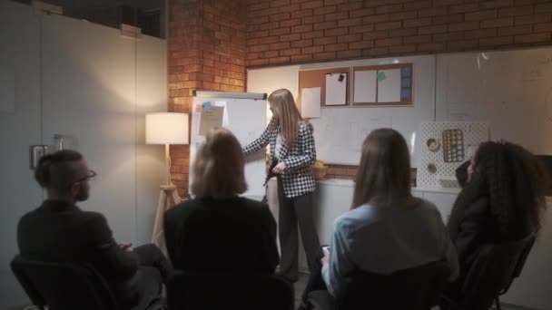 Mujer gerente presenta nuevo plan de proyecto a los colegas en la reunión, explicando las ideas en el rotafolio a los compañeros de trabajo en la oficina, empresaria da la presentación — Vídeo de stock