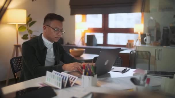 Porträtt av en skäggig arkitekt klädd glasögon sitter i sitt kontor arbetar sent på natten tittar på bildskärm på en dator. Datorskärmen reflekterar i hans glasögon. — Stockvideo