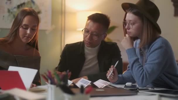 Tres personas elegantes y diversas están sentadas en la mesa mientras discuten enérgicamente el proyecto. Hora de la tarde . — Vídeo de stock