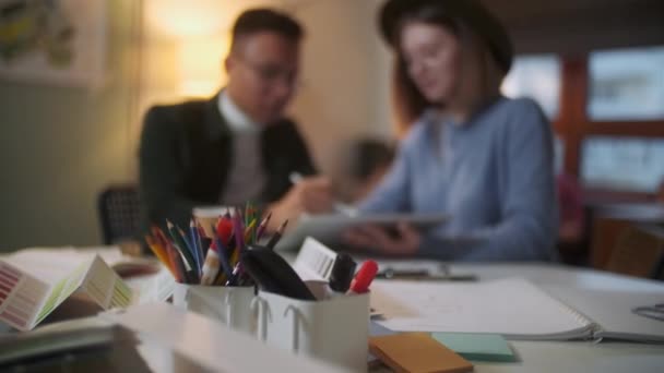 Jóvenes diseñadores con estilo están discutiendo un proyecto en una tableta dibujando con una pluma, fondo femenino y masculino con computadora portátil . — Vídeos de Stock