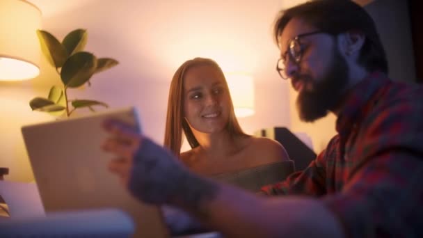 Uomo che parla con il cliente con il computer portatile e tablet discutendo dettagli tecnici su Tablet Computer. Uomo adulto con barba lavora seduto a tavola, utilizza una tavoletta e matita . — Video Stock