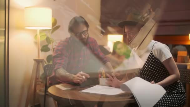 Dos personas elegantes y diversas están sentadas en la mesa mientras discuten enérgicamente el proyecto. Hora de la tarde. Hoja de hombre y mujer a través de la revista del proyecto . — Vídeos de Stock