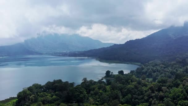 Vista aérea do lago Batur ao pé do vulcão Agung na ilha de Bali, na Indonésia. Drone aéreo voando através de Colinas Florestais Nubladas — Vídeo de Stock