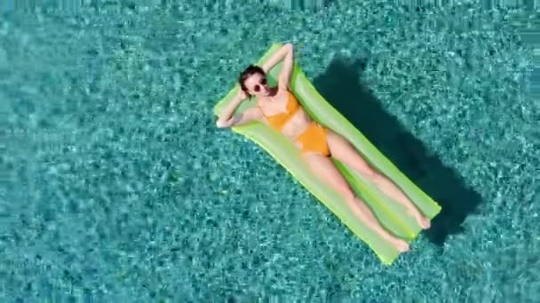 Descanso de mulher sexy e banho de sol em um flutuador verde na piscina, tiro aéreo vista superior. Mulher nova em um terno de banho amarelo do biquíni que flutua em uma vista superior amarela inflável do colchão — Vídeo de Stock