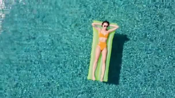 Привлекательная женщина на надувной зеленой платформе в бассейне наслаждаясь летом расслабляясь в отпуске носить сексуальный желтый Бикини — стоковое видео