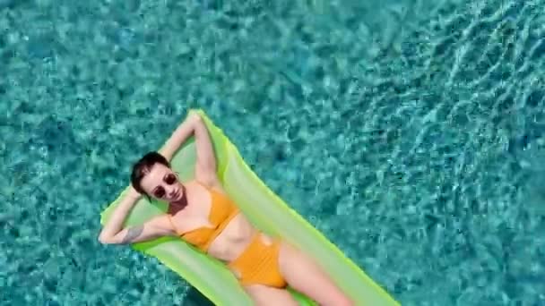Femme attirante sur flotteur vert gonflable dans la piscine profitant de la détente estivale en vacances portant un bikini jaune sexy vue du dessus — Video