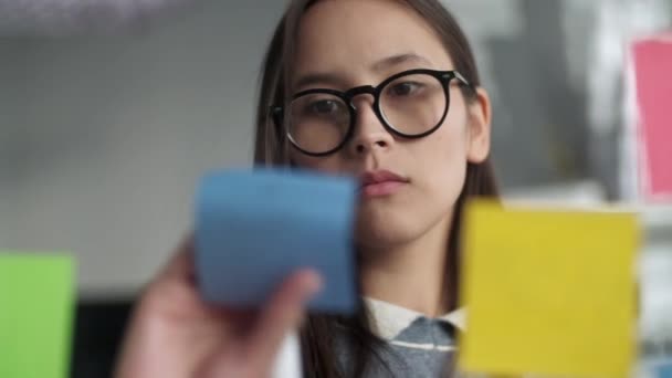 Young Business Woman Brainstorming. Asian Woman Writing Down Ideas On Sticky Notes Attached To Glass Wall. Business Success Concept — Stock Video