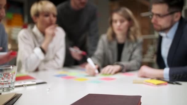 Equipo de negocios lluvia de ideas utilizando etiquetas de color en la mesa en la oficina. Mujer está escribiendo en pegatinas sentado en el escritorio en la habitación de la oficina . — Vídeos de Stock