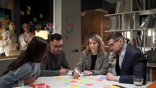 Equipo de negocios lluvia de ideas utilizando etiquetas de color en la mesa en la oficina. Mujer está escribiendo en pegatinas sentado en el escritorio en la habitación de la oficina . — Vídeos de Stock