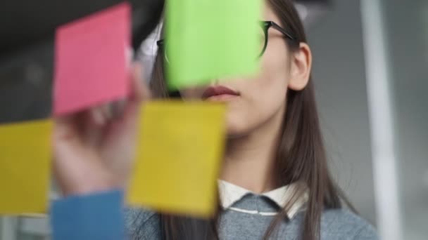 Genç İş Kadını Beyin Fırtınası. Cam duvara yapıştırılmış yapışkan notlara fikir yazan Asyalı kadın. İş Başarı Konsepti — Stok video
